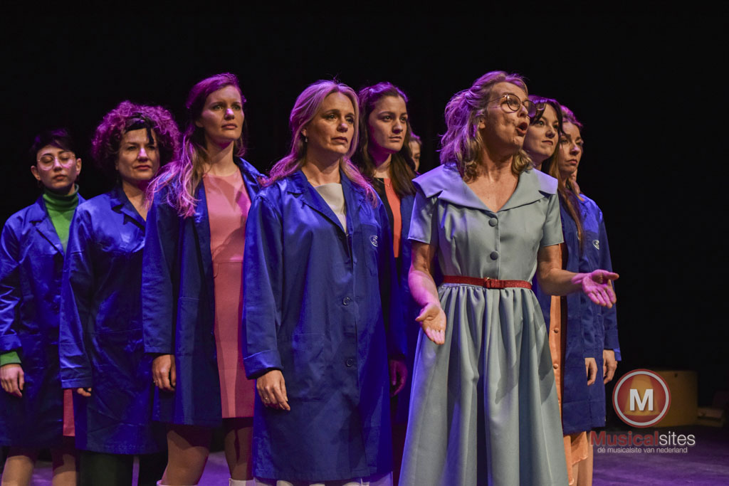 Foto van de Ford werksters in blauwe stofjassen die achter Connie staan in een strijdbare V-vorm.